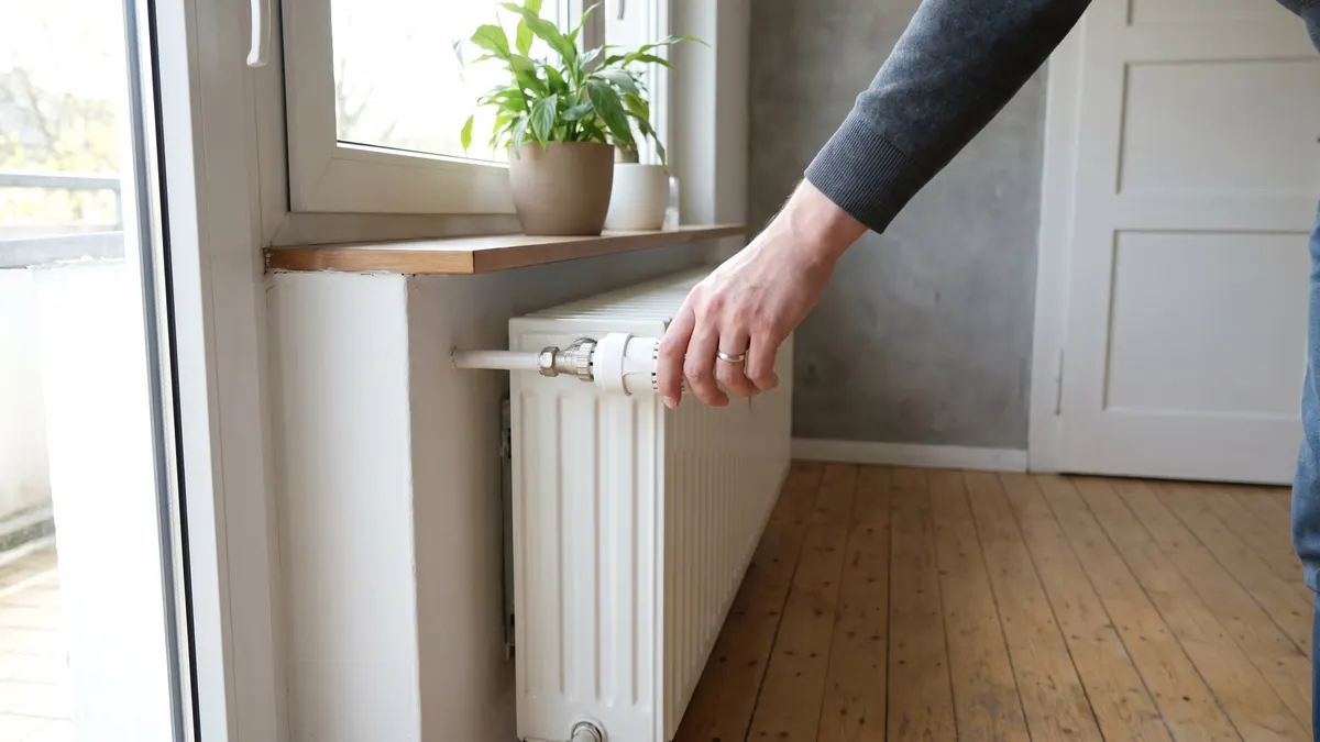 Hand dreht den Thermostatkopf an einem Heizkörper im Wohnzimmer – Fußbodenheizung wird nicht warm