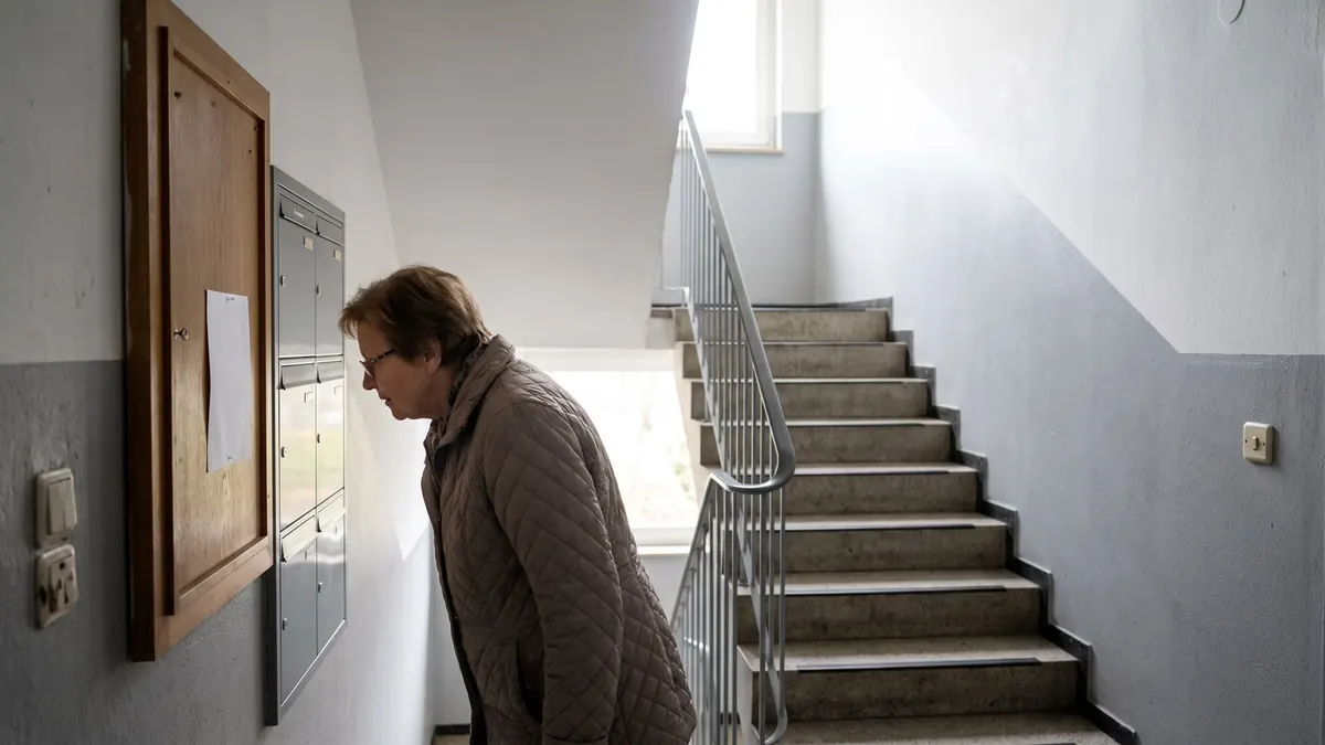 Bewohnerin liest im Treppenhaus eines Mehrfamilienhauses einen Aushang am Brett – Kleines Mehrfamilienhaus mit einem