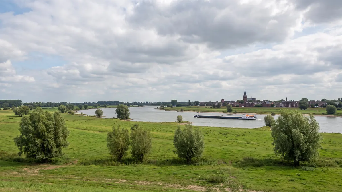 Blick über die Rheinauen am Niederrhein mit Lastkahn und Stadtsilhouette – Heizung in Städten von Rhein bis Wupper